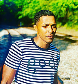 Black man on train tracks wearing black and white striped shirt